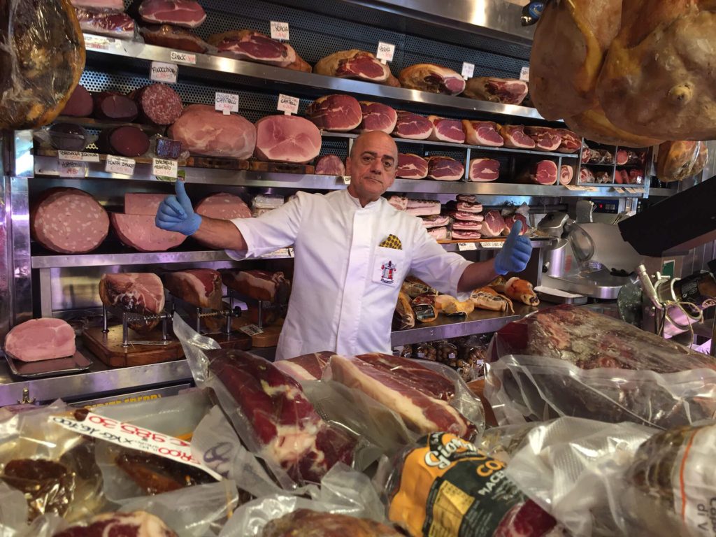 Butcher shop in Rome with gentleman behind the butcher counter that displays various meats in Rome